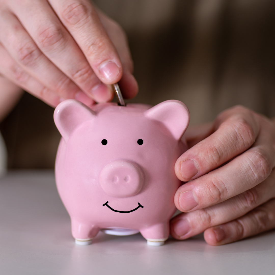 Hands placing a coin into a pink piggy bank